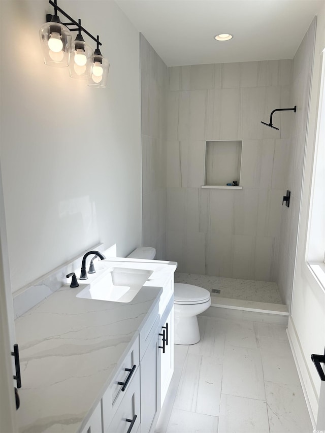 bathroom featuring marble finish floor, tiled shower, vanity, and toilet