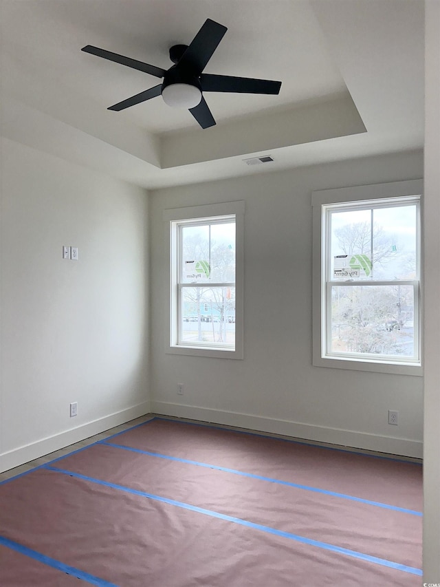 unfurnished room with a tray ceiling, visible vents, ceiling fan, and baseboards