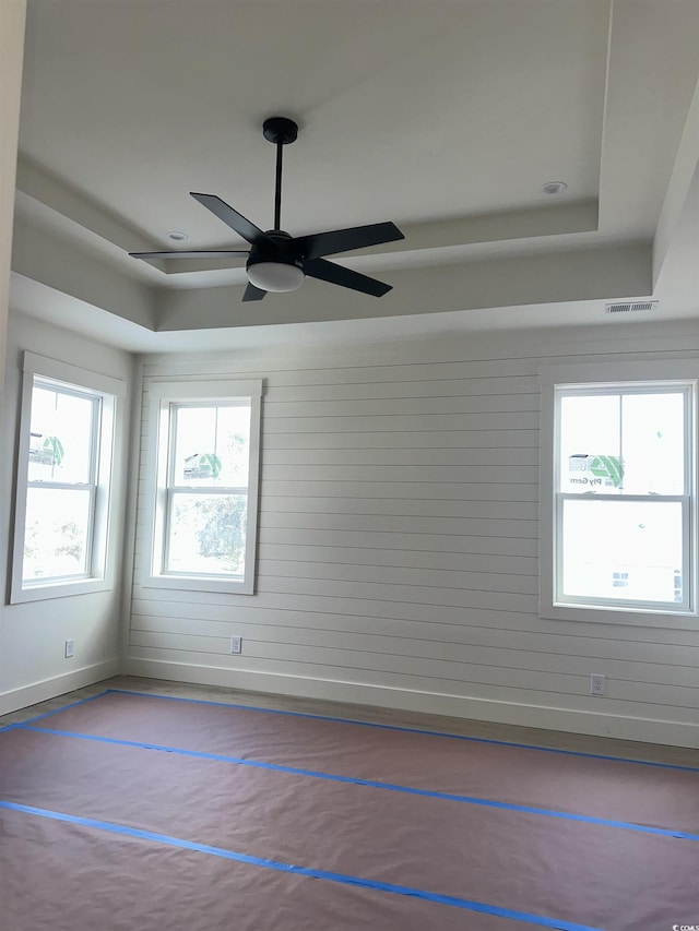 unfurnished room with a tray ceiling, visible vents, ceiling fan, and baseboards