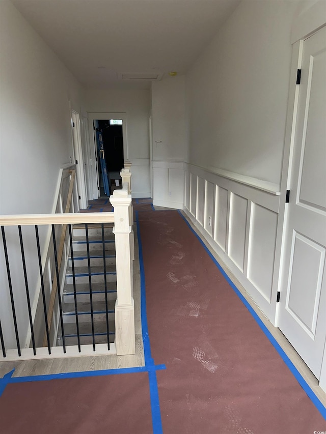 hall with wainscoting, a decorative wall, and an upstairs landing