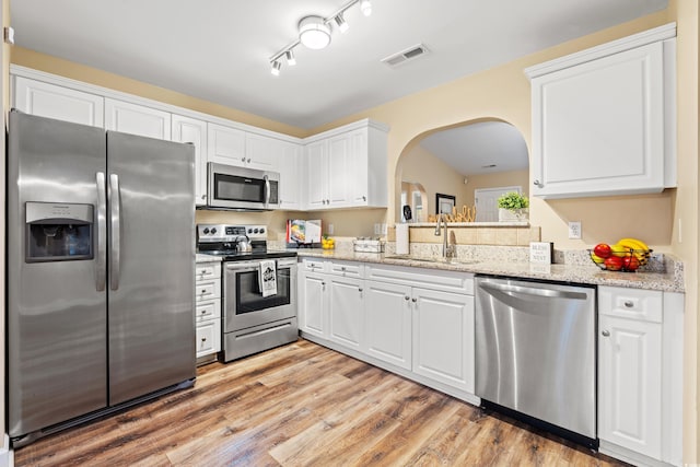 kitchen with stainless steel appliances, a sink, white cabinetry, and light stone countertops