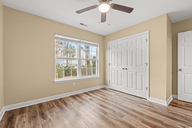 unfurnished bedroom featuring a closet, visible vents, ceiling fan, wood finished floors, and baseboards