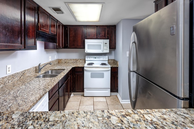 kitchen featuring visible vents, a sink, light stone countertops, white appliances, and baseboards