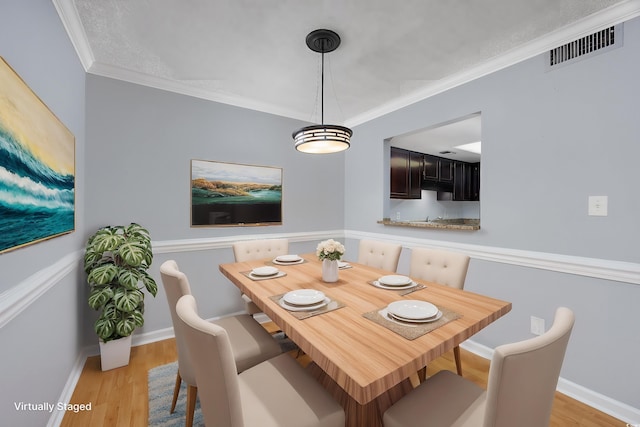 dining room featuring baseboards, light wood-style flooring, visible vents, and crown molding