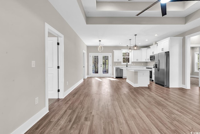 kitchen featuring a kitchen island, white cabinetry, stainless steel appliances, light countertops, and baseboards