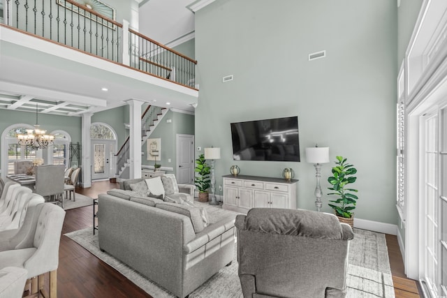 living area featuring a high ceiling, coffered ceiling, wood finished floors, stairway, and an inviting chandelier