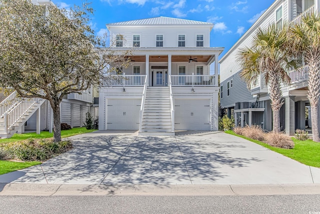 coastal inspired home featuring a ceiling fan, metal roof, an attached garage, covered porch, and stairs