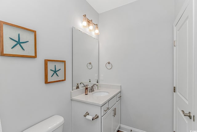 half bathroom with baseboards, vanity, and toilet