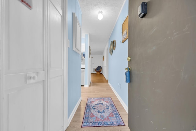 hallway featuring light wood-type flooring, baseboards, and a textured ceiling