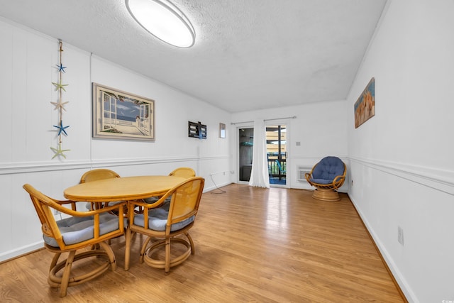 dining room featuring baseboards, a textured ceiling, and light wood finished floors