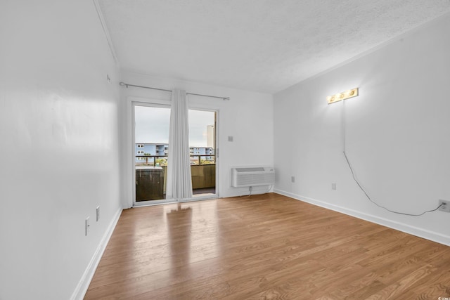 spare room with light wood finished floors, baseboards, a textured ceiling, and a wall mounted air conditioner