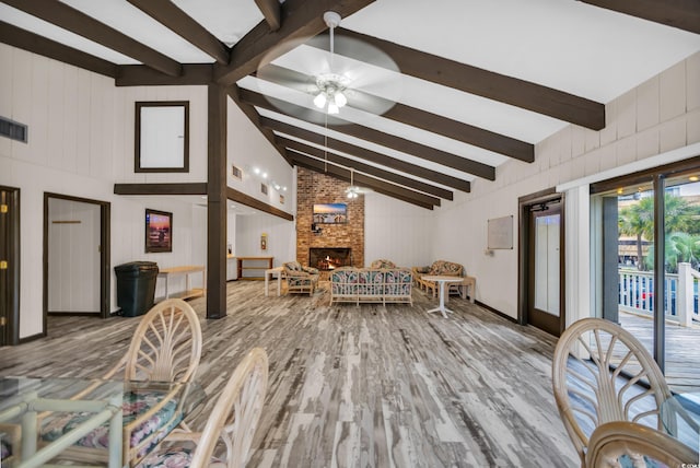 living area featuring ceiling fan, beamed ceiling, wood finished floors, a fireplace, and high vaulted ceiling