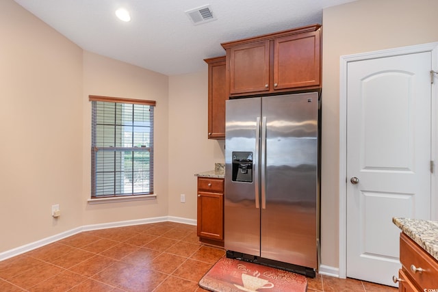 kitchen with brown cabinets, visible vents, stainless steel fridge with ice dispenser, and light stone countertops