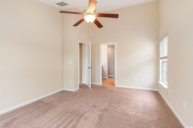 spare room featuring light colored carpet, a towering ceiling, visible vents, and baseboards