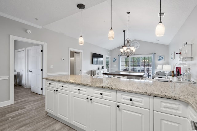 kitchen featuring light stone counters, light wood-style floors, open floor plan, white cabinets, and pendant lighting