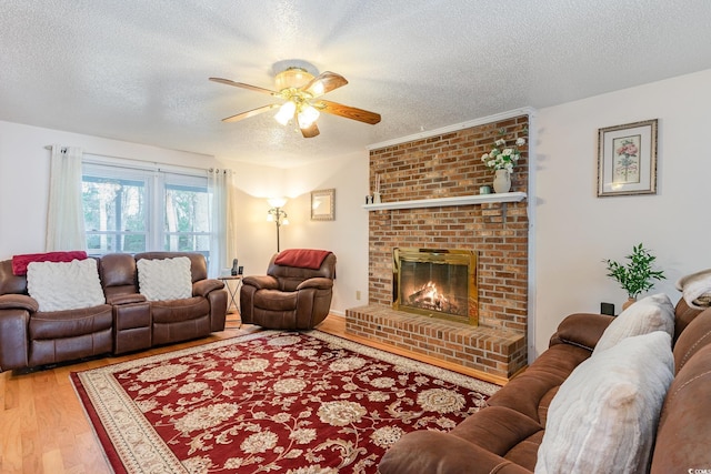 living area with a textured ceiling, a ceiling fan, wood finished floors, and a fireplace