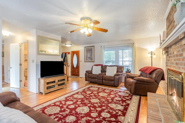 living room featuring a fireplace, light wood-type flooring, a textured ceiling, and ceiling fan