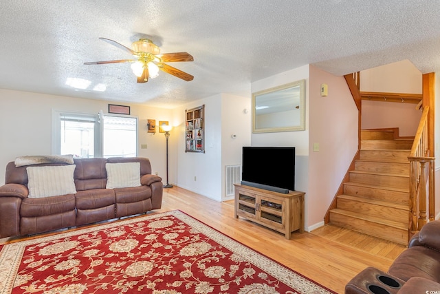 living area with light wood-type flooring, a textured ceiling, a ceiling fan, visible vents, and stairway