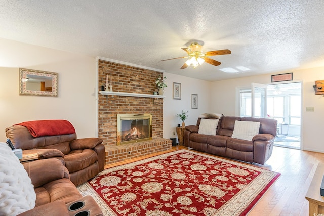 living area with wood-type flooring, ceiling fan, a brick fireplace, and a textured ceiling