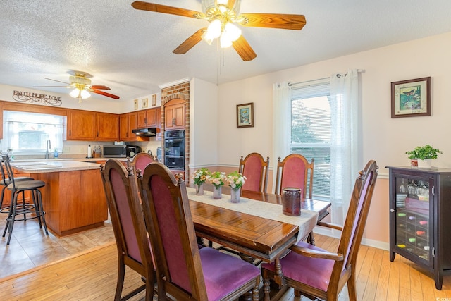 dining room with baseboards, a textured ceiling, a ceiling fan, wine cooler, and light wood finished floors