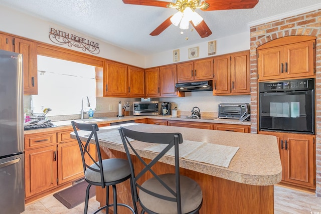kitchen with black appliances, under cabinet range hood, light countertops, a sink, and a toaster