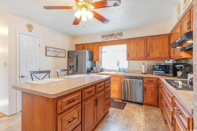 kitchen with light countertops, under cabinet range hood, brown cabinetry, ceiling fan, and stainless steel appliances