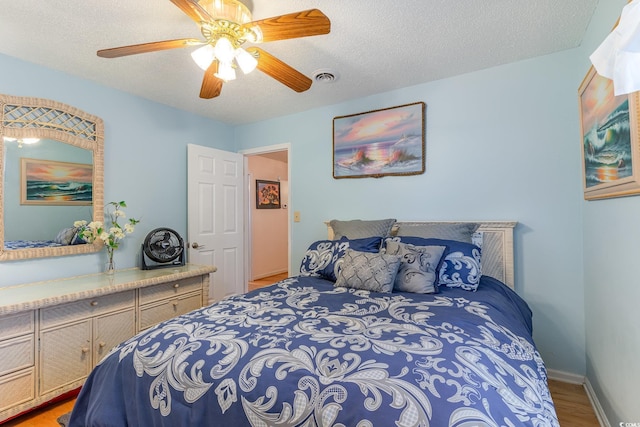 bedroom featuring baseboards, light wood-style flooring, a textured ceiling, a ceiling fan, and visible vents