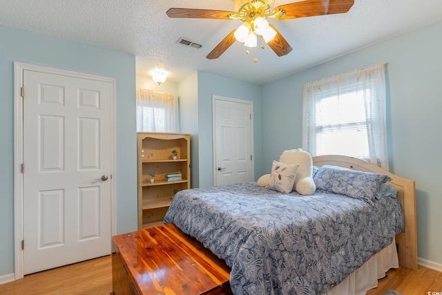 bedroom with light wood-style floors, a textured ceiling, a ceiling fan, visible vents, and baseboards