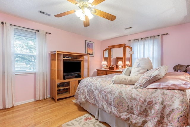 bedroom with light wood finished floors, visible vents, a textured ceiling, and a ceiling fan