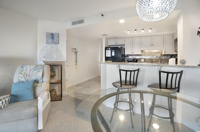 kitchen with tasteful backsplash, visible vents, freestanding refrigerator, white cabinetry, and a peninsula