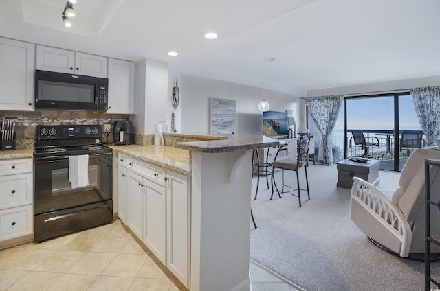 kitchen with a breakfast bar area, open floor plan, white cabinetry, a peninsula, and black appliances