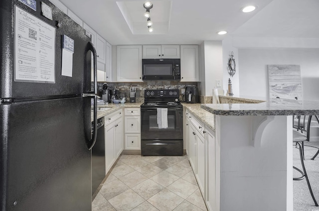 kitchen featuring light stone counters, a peninsula, a breakfast bar, decorative backsplash, and black appliances