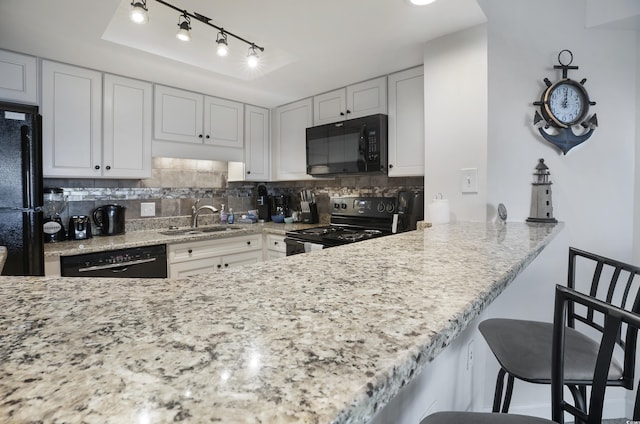 kitchen featuring a kitchen bar, decorative backsplash, white cabinets, a sink, and black appliances