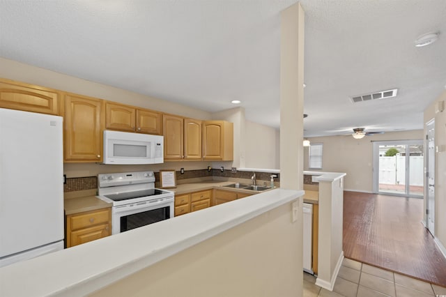 kitchen featuring a peninsula, white appliances, a sink, visible vents, and light brown cabinetry