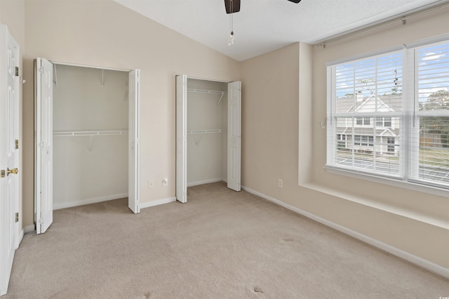 unfurnished bedroom with baseboards, light colored carpet, ceiling fan, vaulted ceiling, and multiple closets