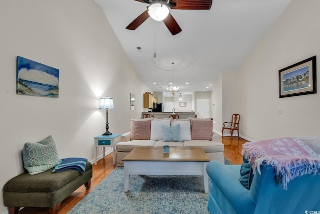 living area with lofted ceiling, ceiling fan with notable chandelier, visible vents, baseboards, and light wood finished floors