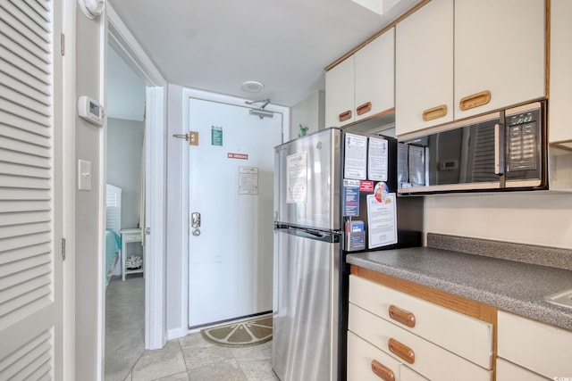 kitchen featuring light tile patterned floors, dark countertops, freestanding refrigerator, and white cabinetry