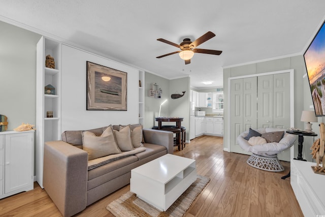 living room with light wood-type flooring, built in features, a ceiling fan, and crown molding