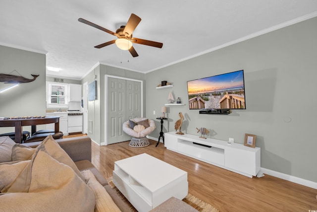 living area with ornamental molding, light wood-type flooring, baseboards, and a ceiling fan