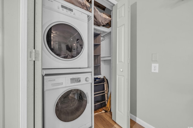 laundry room featuring stacked washer and dryer, laundry area, baseboards, and light wood finished floors