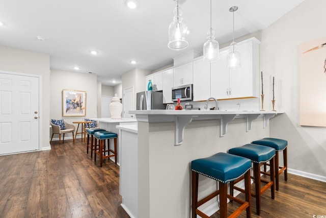 kitchen with stainless steel appliances, light countertops, a kitchen bar, white cabinetry, and pendant lighting