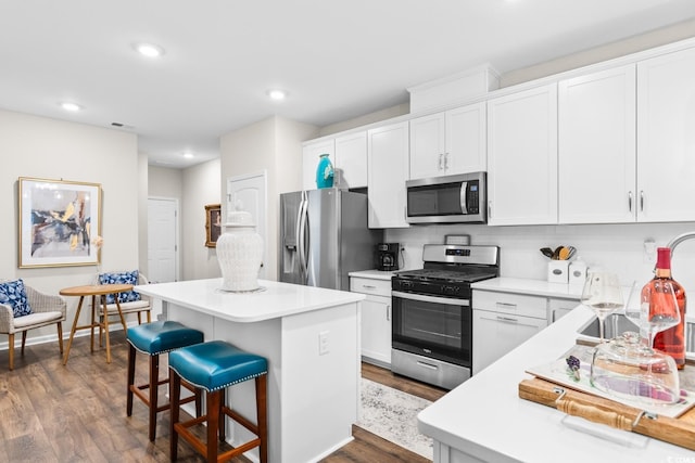 kitchen with stainless steel appliances, a kitchen island, white cabinetry, a kitchen breakfast bar, and light countertops