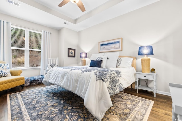 bedroom featuring a tray ceiling, visible vents, a ceiling fan, wood finished floors, and baseboards