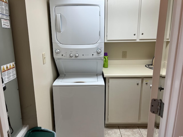 clothes washing area with stacked washer and dryer, light tile patterned flooring, gas water heater, and cabinet space