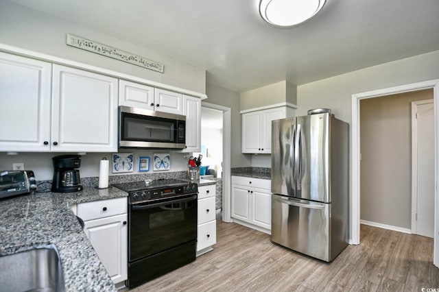 kitchen featuring appliances with stainless steel finishes, dark stone counters, white cabinetry, and light wood-style floors