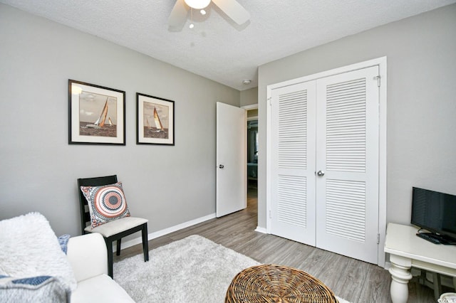 interior space with light wood-type flooring, a ceiling fan, baseboards, and a textured ceiling