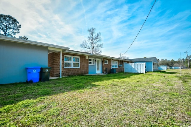 rear view of house featuring fence, a lawn, and brick siding