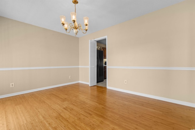 empty room featuring an inviting chandelier, baseboards, and wood finished floors