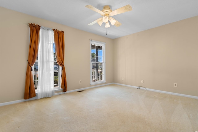 empty room featuring a ceiling fan, light carpet, visible vents, and baseboards