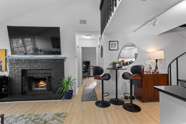 interior space with lofted ceiling, wood finished floors, visible vents, a brick fireplace, and track lighting